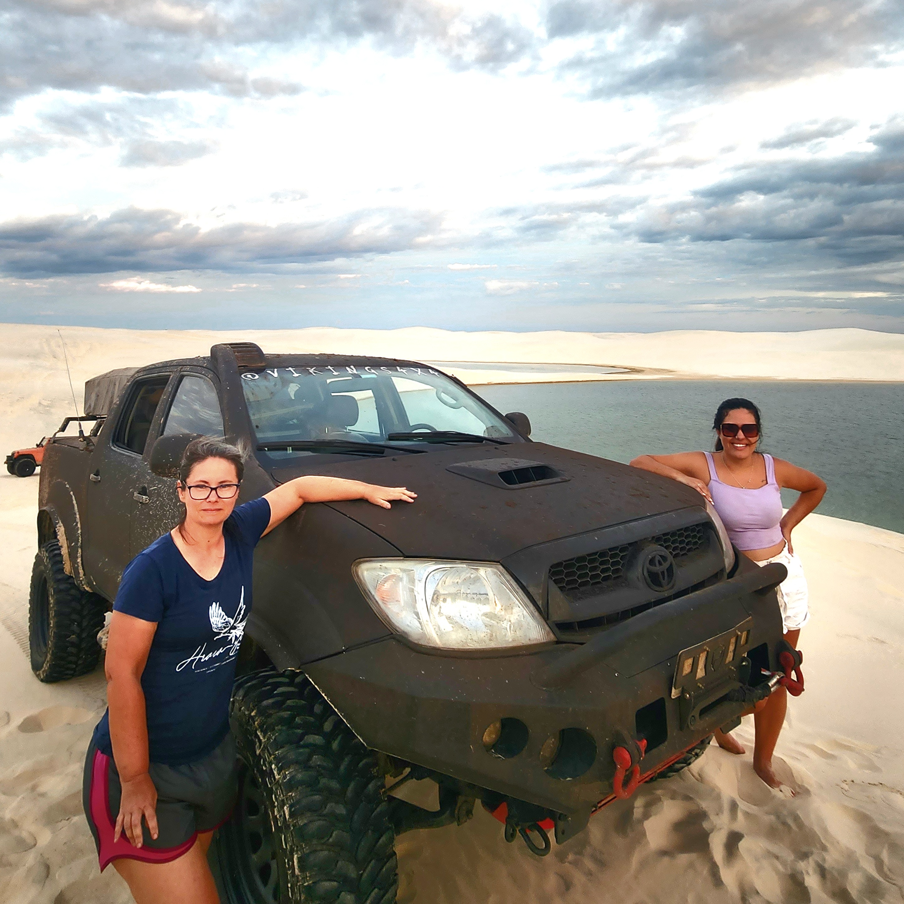 Toyota Hilux 3.0 2009 em cenário de areia e lagoas com duas pessoas ao lado